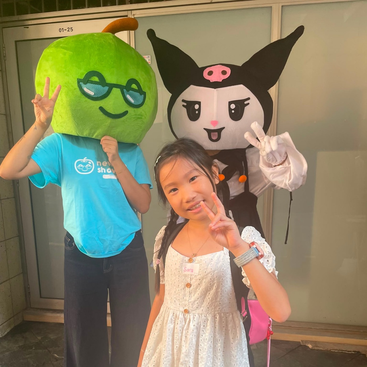 Two Newtonshow mascots posing with a smiling camper outside a Hong Kong campus