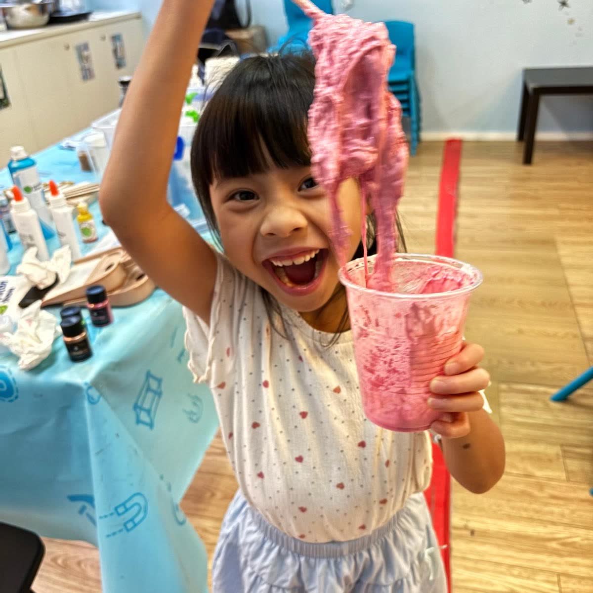 Delighted girl holding up a long strand of bright pink slime she made at a Newtonshow Hong Kong camp